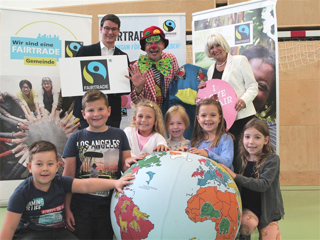 FairTrade Clown Hugo mit Florian Scheicher, Rosa Bock und den Kindern der VS Stadt, die „un-sere Welt“ in Händen halten.